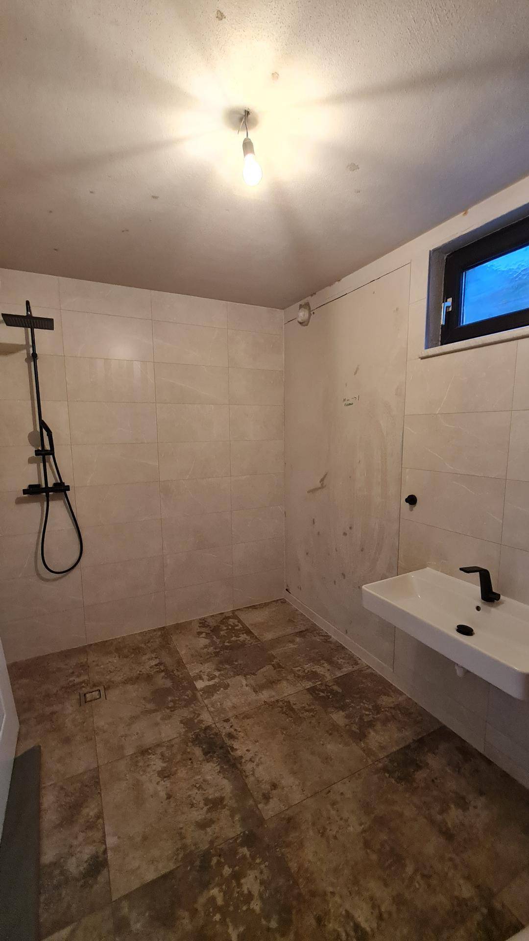 Modernes Badezimmer mit großer Dusche, Fenster und Fliesenboden.