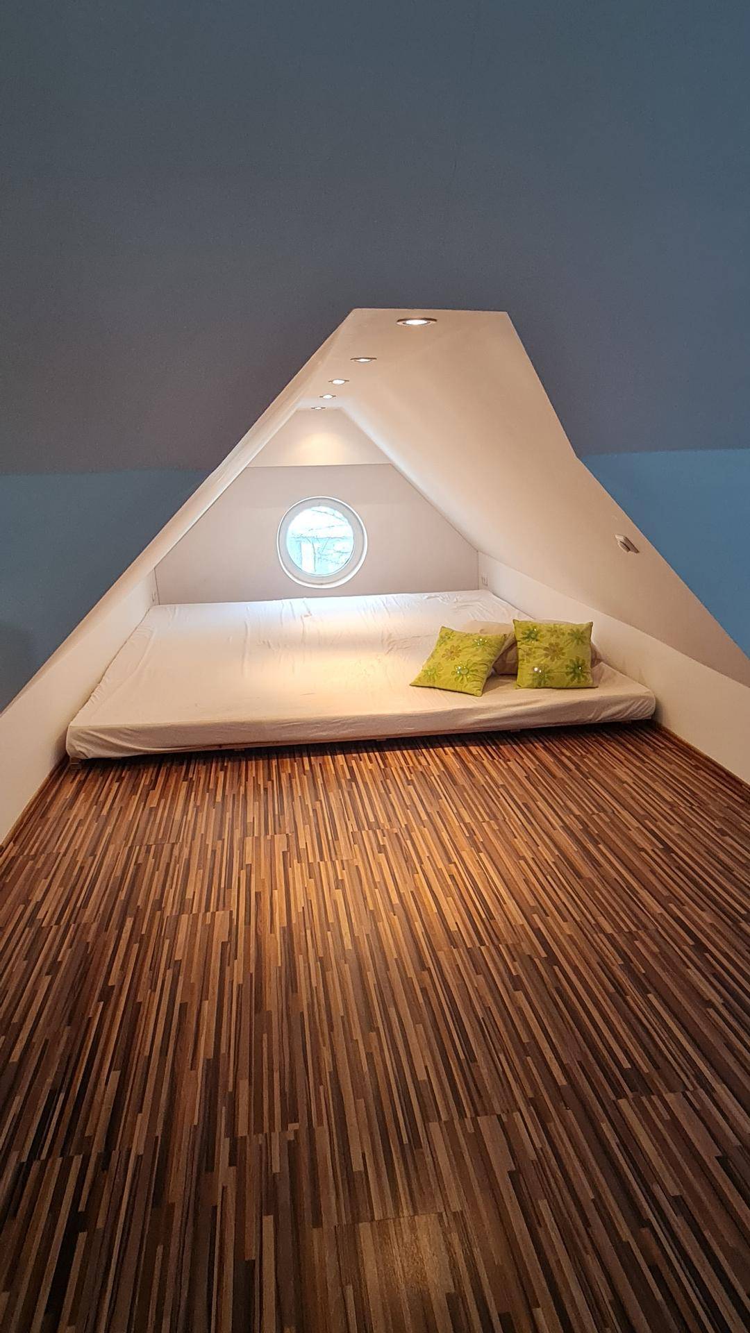 Gemütlicher Schlafbereich im Dachgeschoss mit Holzboden und rundem Fenster.