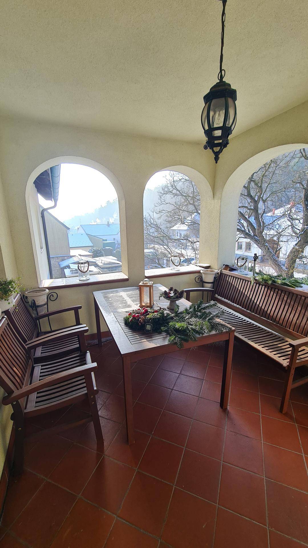 Gemütlicher Wintergarten mit Holztisch, Sitzgelegenheiten und Blick ins Grüne.