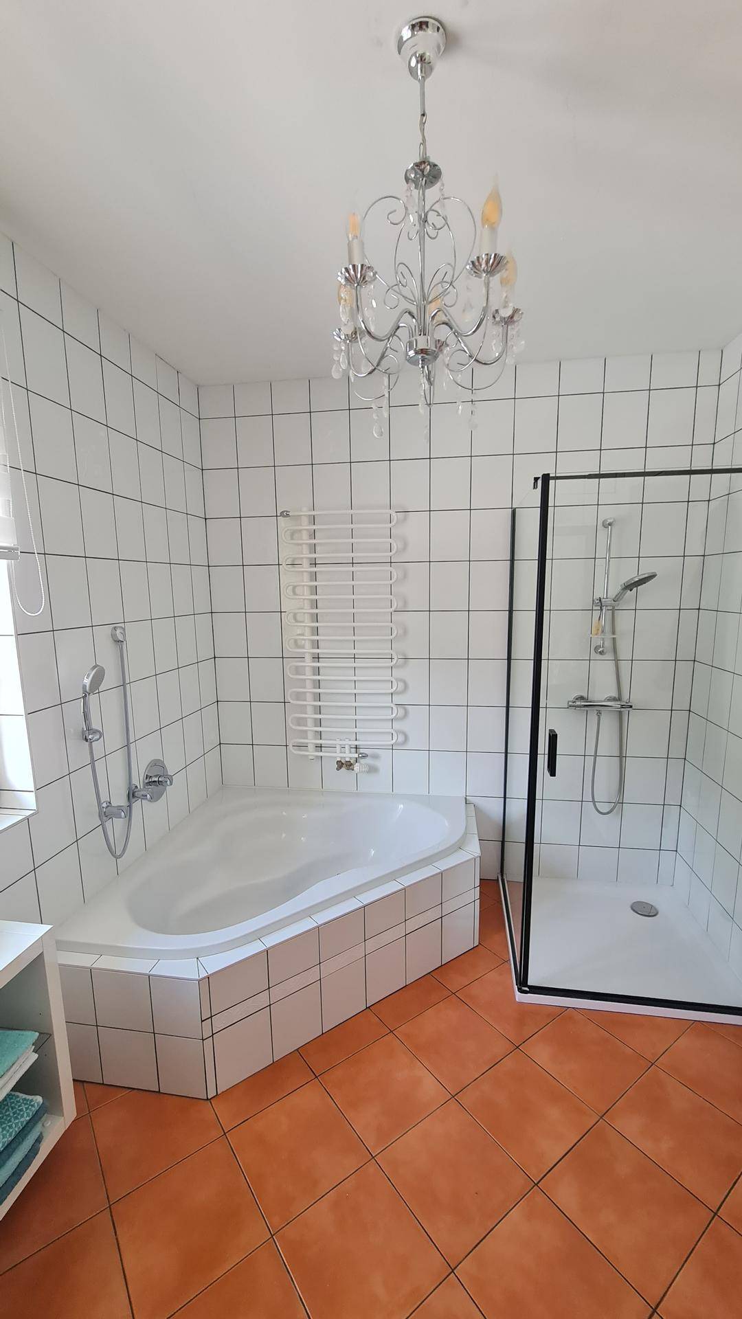 Badezimmer mit Eckbadewanne, Duschkabine, weißen Fliesen und Terrakotta-Boden.
