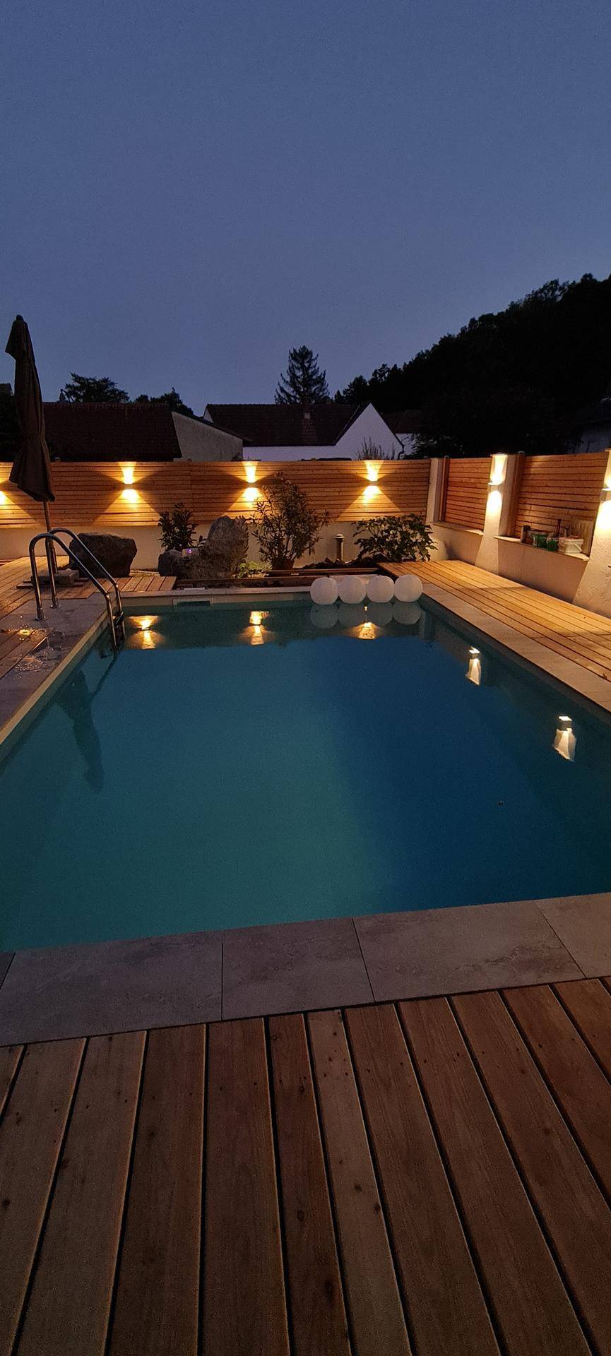 Beleuchteter Außenpool bei Nacht mit Holzdeck und stimmungsvoller Beleuchtung.