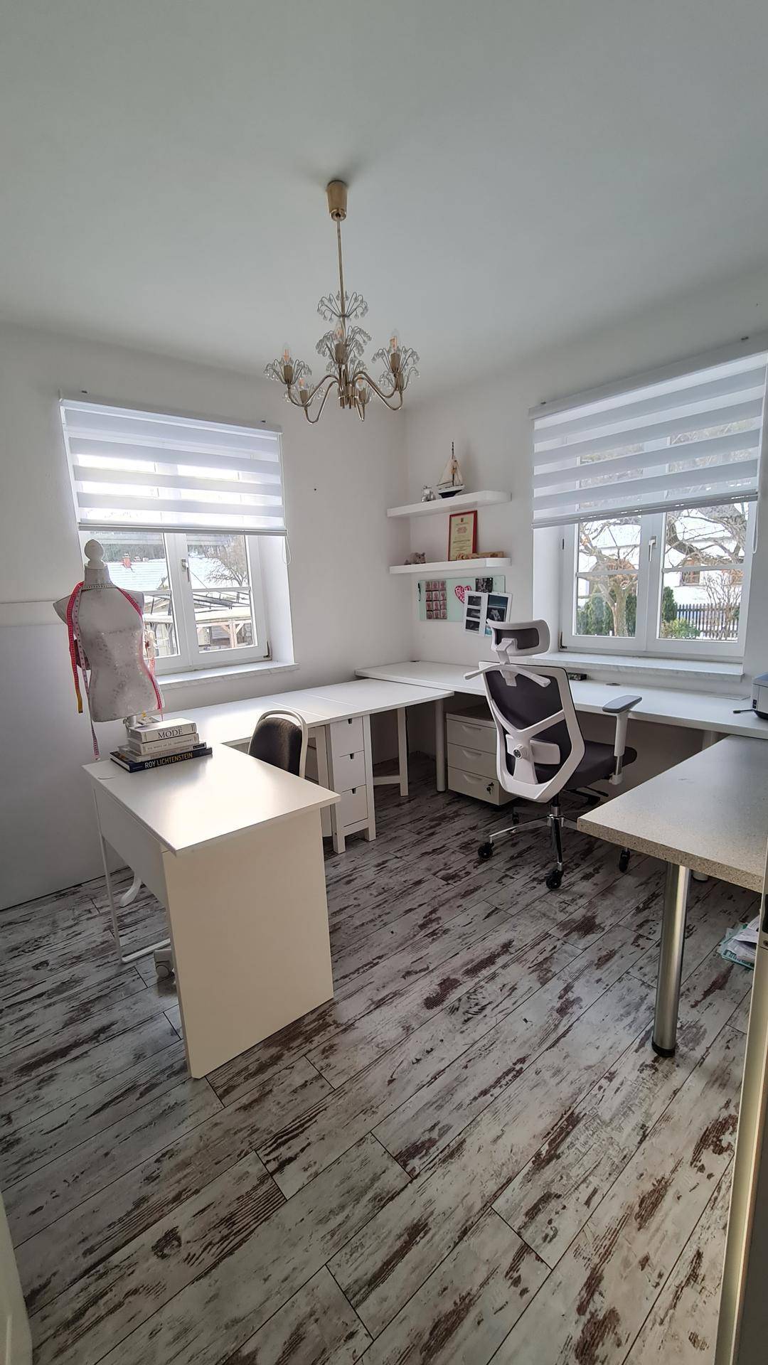 Helles Büro mit zwei Fenstern, Schreibtischen und Holzboden.