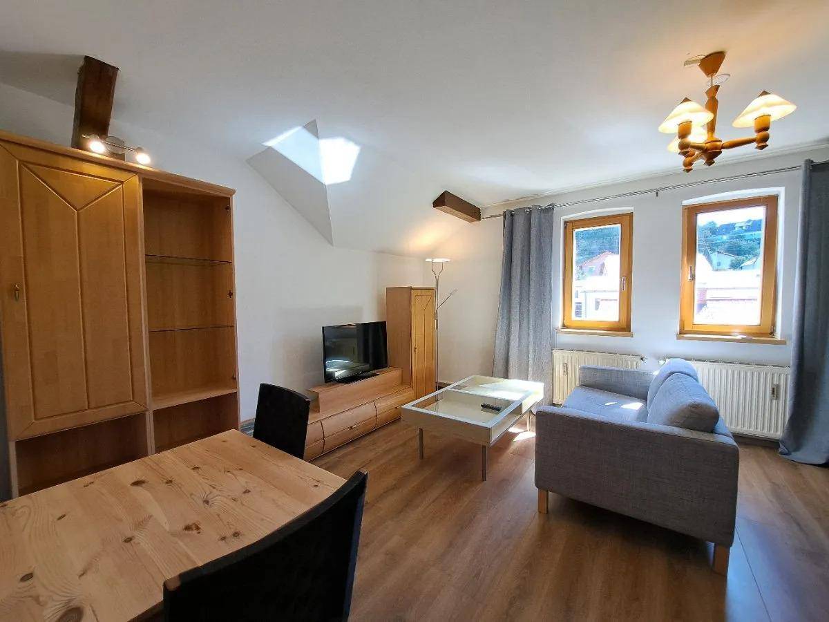 Wohn-Essbereich mit Holzboden, zwei Fenstern, Sofa und Esstisch, der viel Tageslicht hereinlässt.
