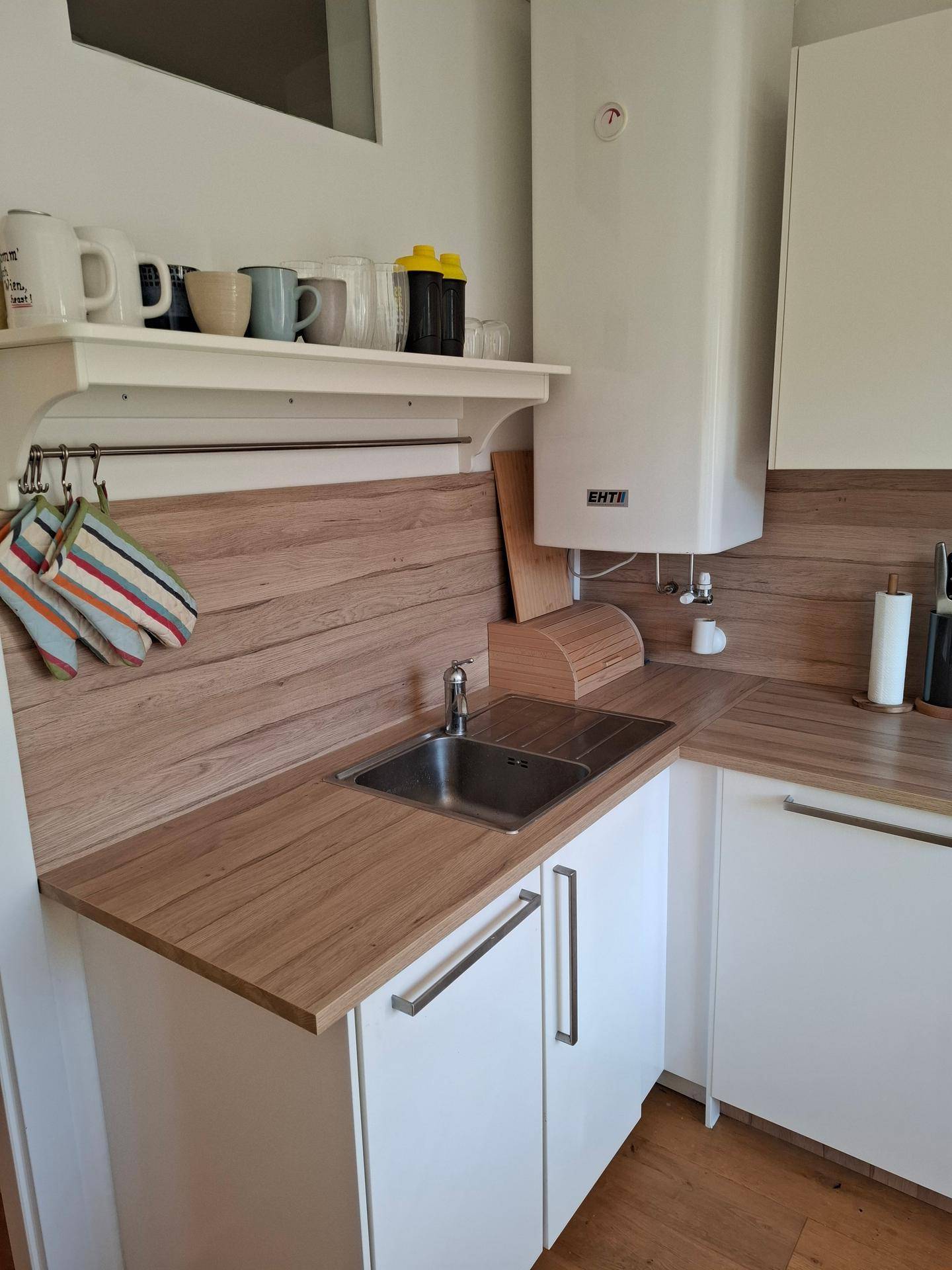 Küchenzeile mit Spüle, Holzarbeitsplatte und Warmwasserboiler an der Wand.