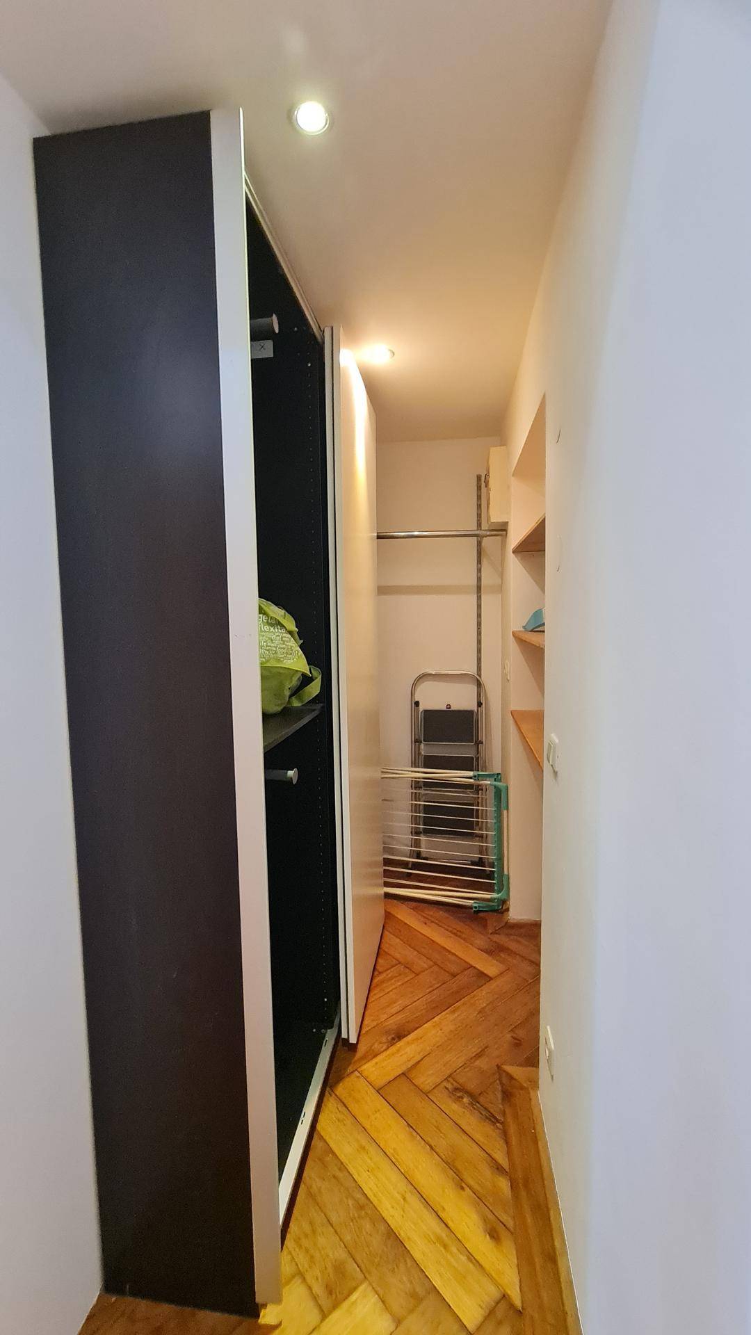 Begehbarer Kleiderschrank mit Regalen und Kleiderstangen auf Parkettboden.