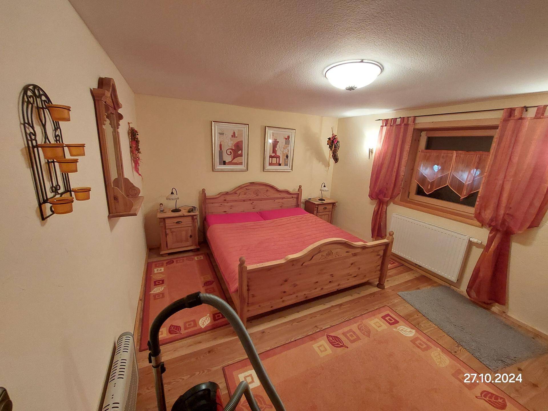 Rustikales Schlafzimmer mit Holzbett, Nachttischen und einem Fenster mit traditionellen Vorhängen.