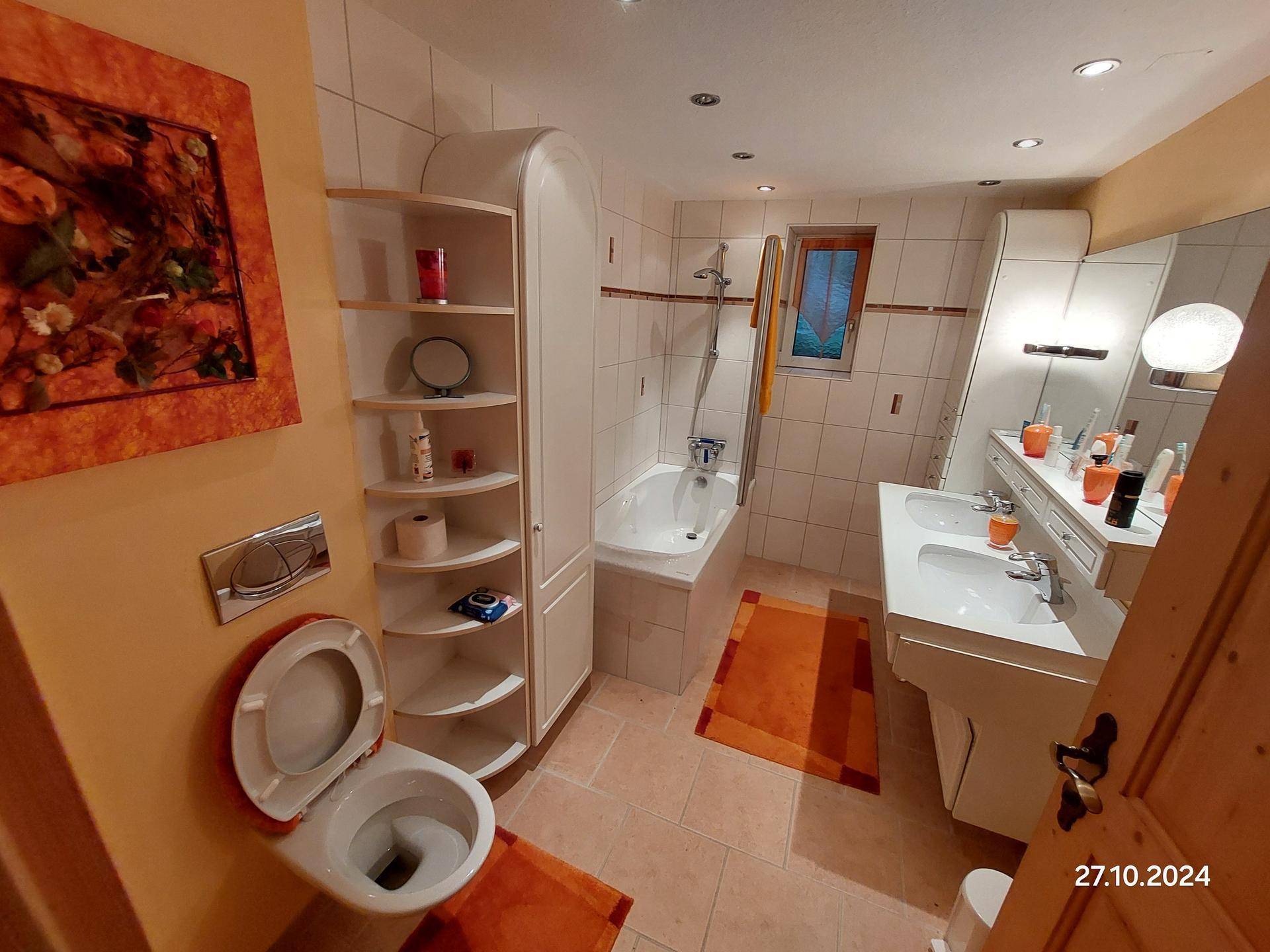 Badezimmer mit Doppelwaschbecken, Badewanne, Toilette und orangefarbenen Akzenten.