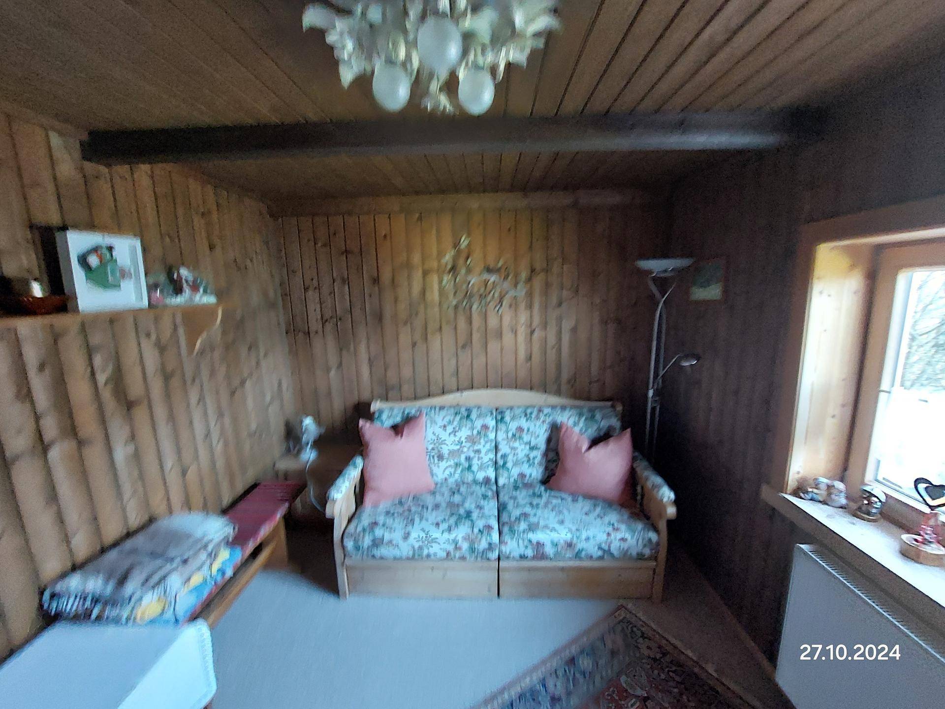 Gemütliches Wohnzimmer mit Holzvertäfelung, floralem Sofa und natürlichem Lichteinfall.