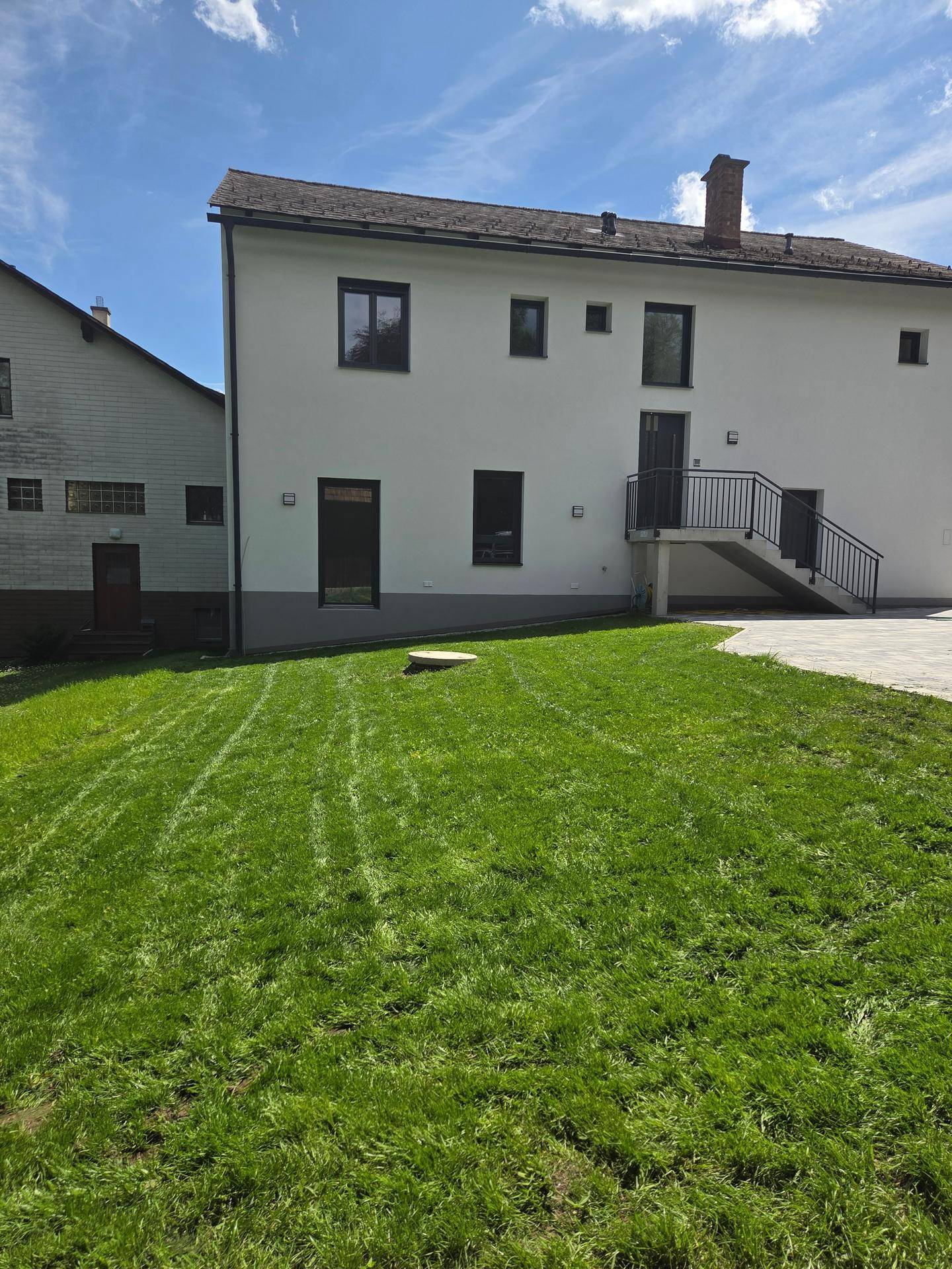 Gepflegter Gartenbereich hinter dem Haus mit frischem Rasen und Außentreppe zum Obergeschoss.