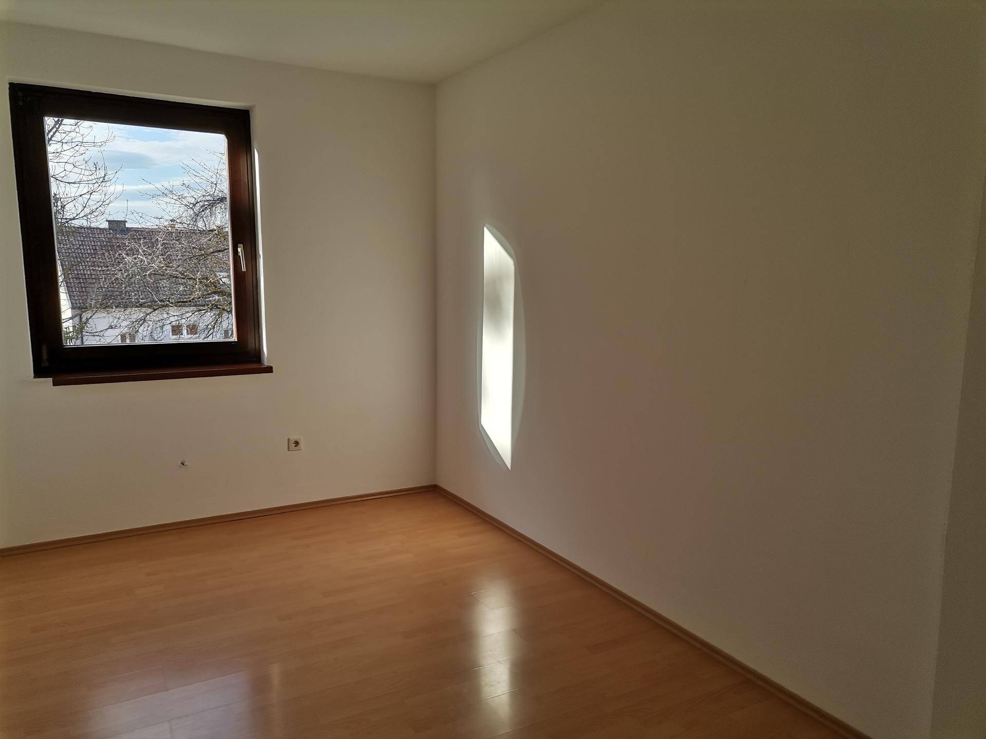 Helles Zimmer mit Laminatboden und einem Fenster, das viel Tageslicht hereinlässt.