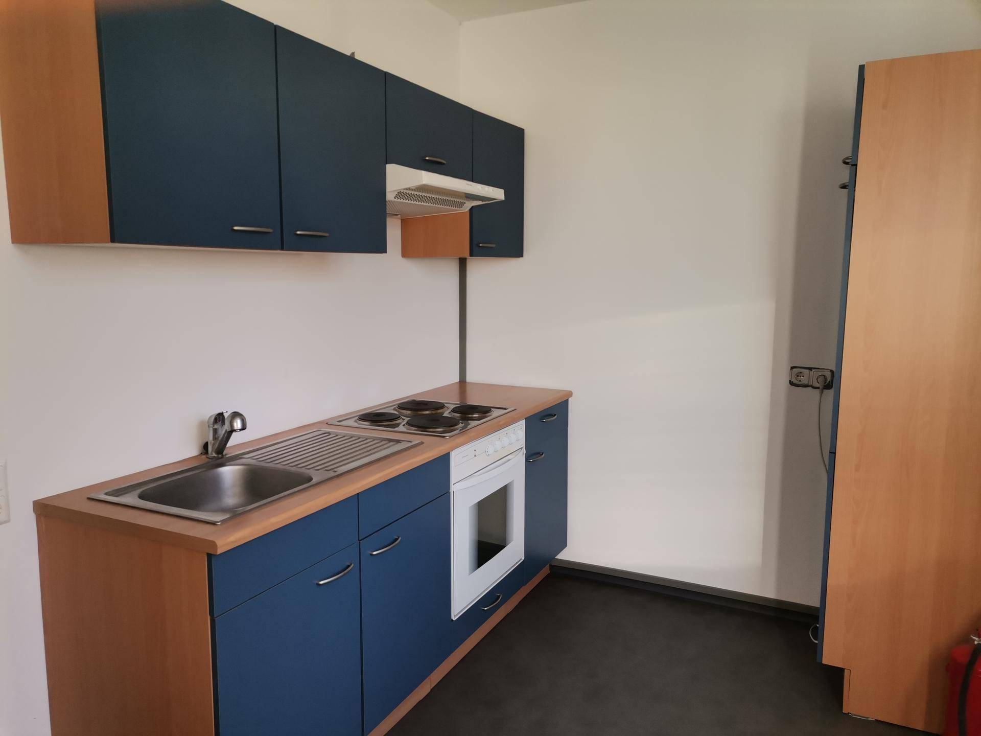 Kleine Küche mit blauen Schränken, Holztheke und integriertem Herd und Spüle.