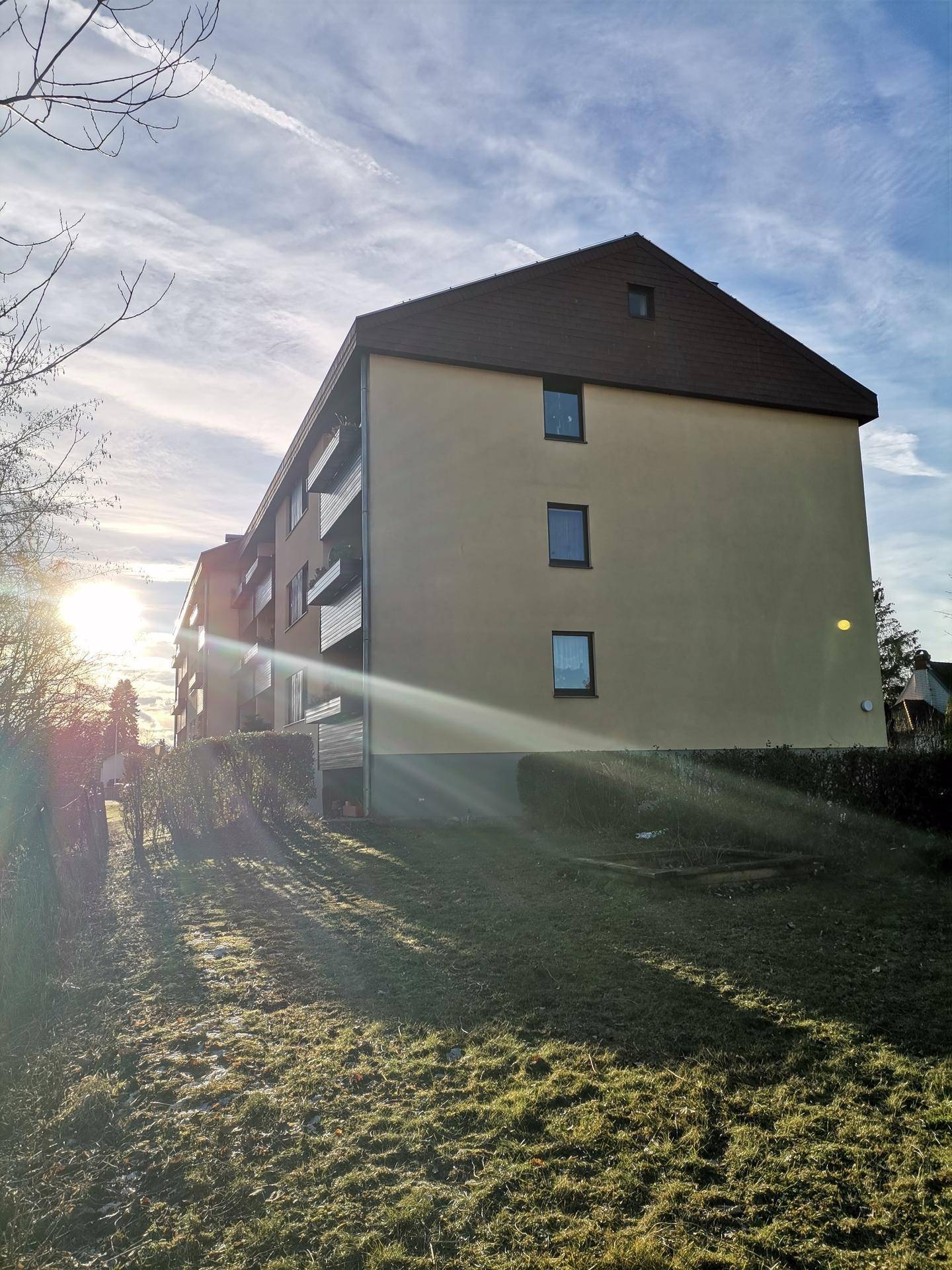 Seitenansicht eines Mehrfamilienhauses mit gelber Fassade und braunem Dach bei Sonnenuntergang.