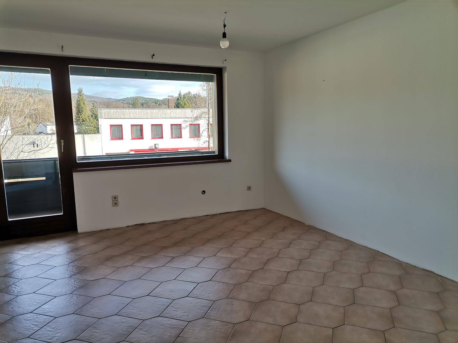 Heller Wohnbereich mit Fliesenboden und großen Fenstern mit Blick auf die Umgebung.