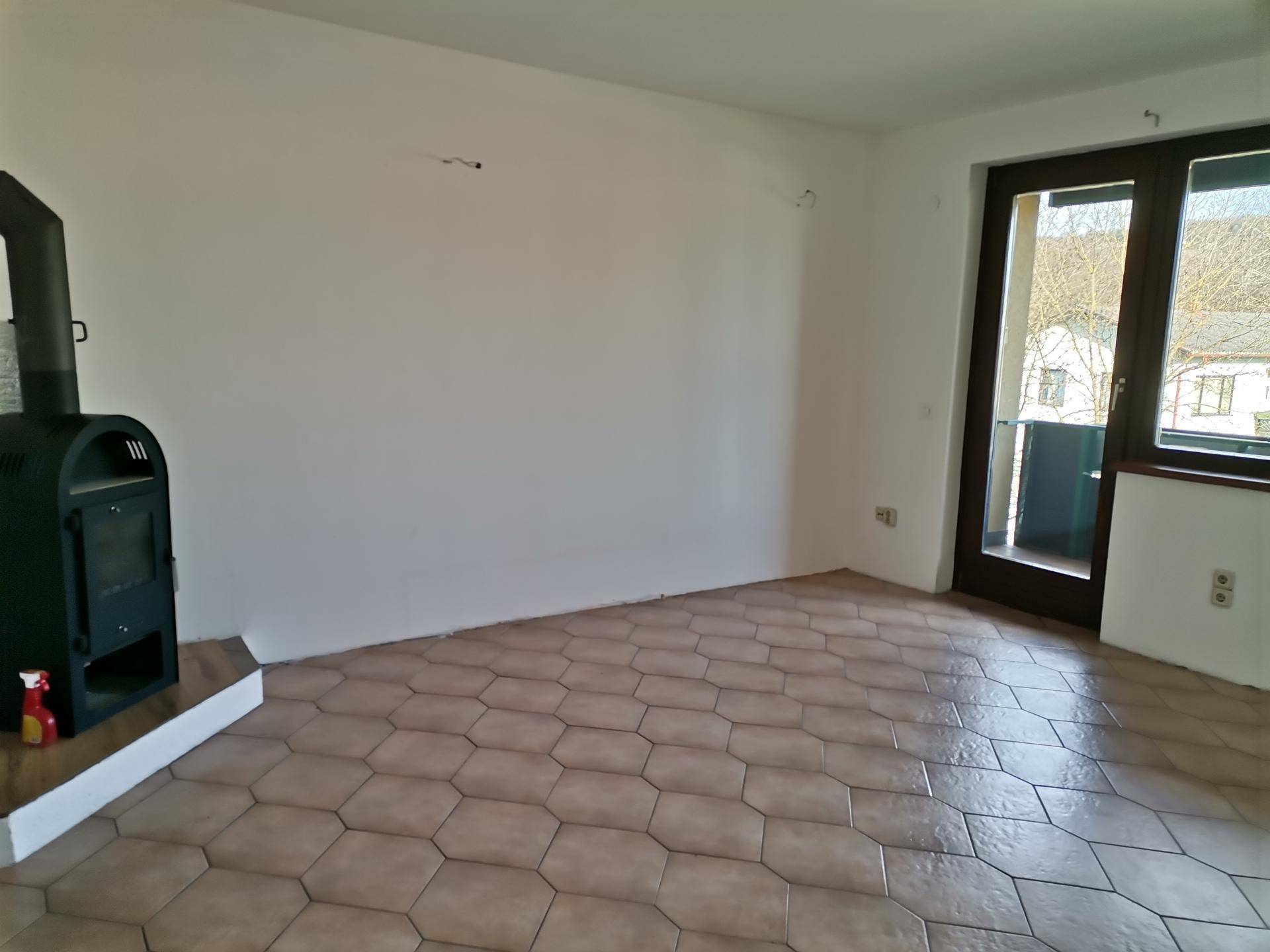 Wohnzimmer mit Kaminofen, Fliesenboden und Zugang zu einem Balkon.