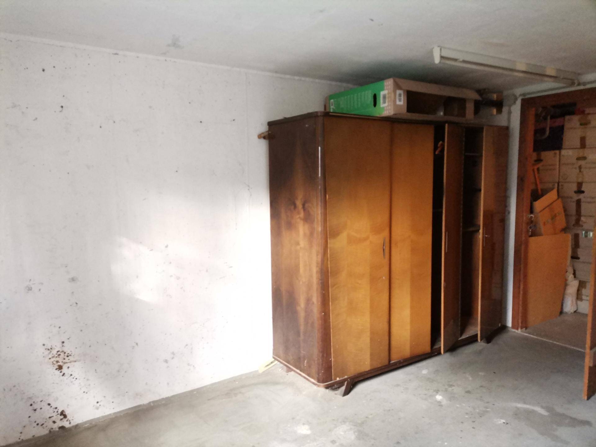 Abstellraum im Keller mit einem alten Holzschrank und Betonboden.