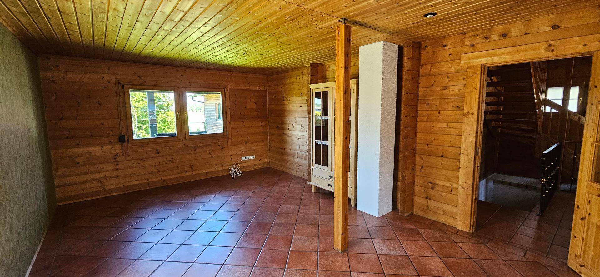 Geräumiger Wohnbereich mit Holzvertäfelung, Terrakottafliesen und großem Fenster.