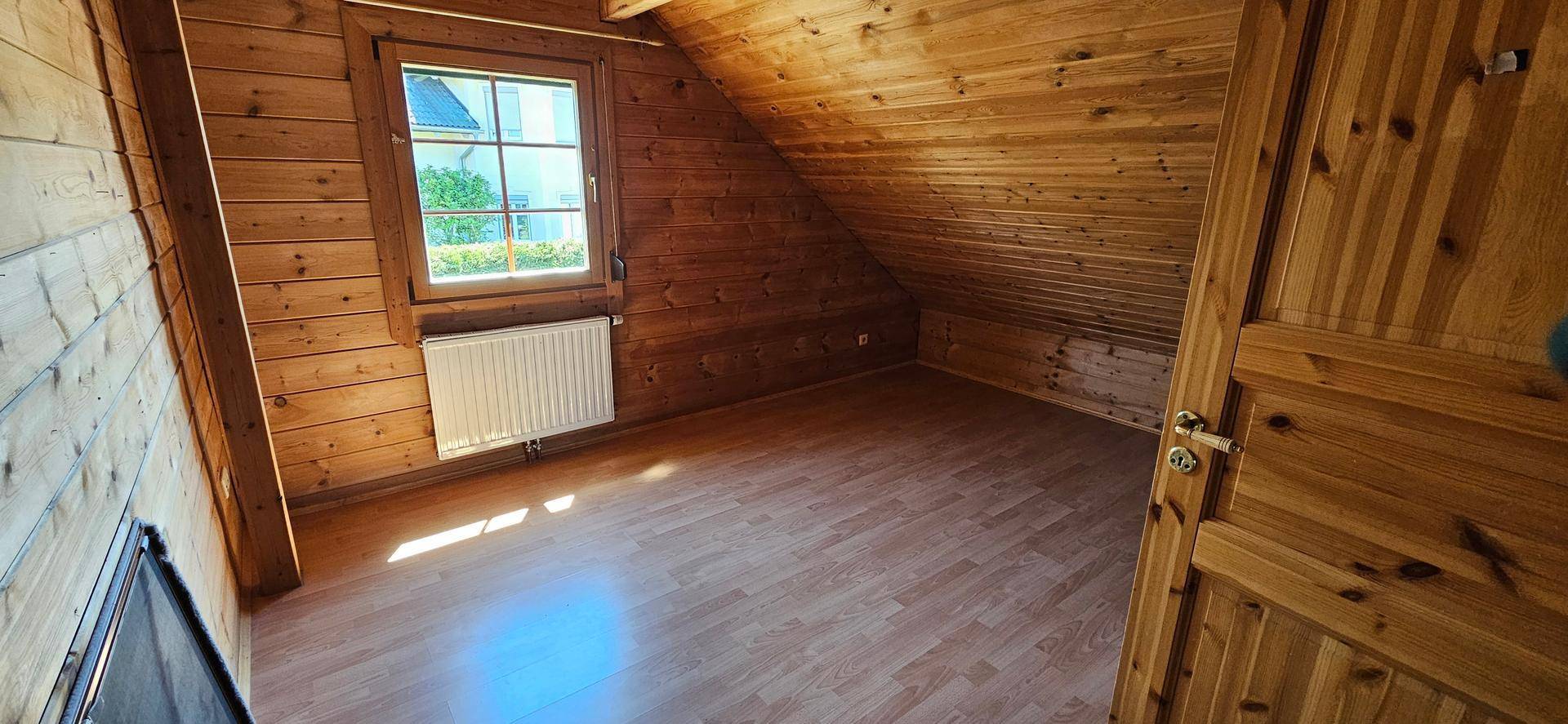Gemütliches Dachgeschosszimmer mit Holzvertäfelung, Laminatboden und Fenster.