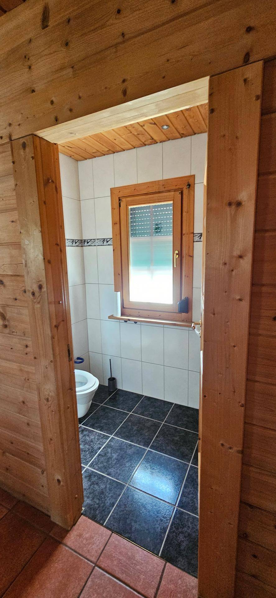 Kleines Gäste-WC mit weißen Wandfliesen und dunklen Bodenfliesen.