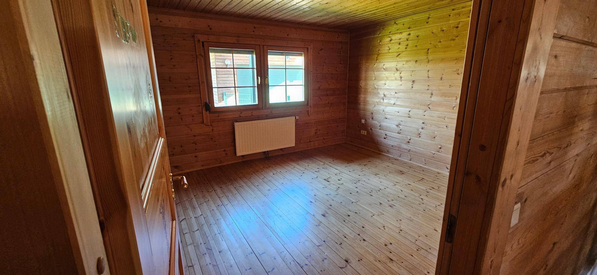Gemütliches Schlafzimmer mit Holzvertäfelung, Holzboden und Fenster für natürliches Licht.