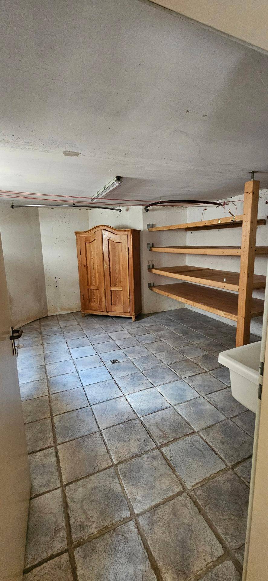 Geräumiger Abstellraum im Keller mit Fliesenboden, Holzregalen und einem Schrank.