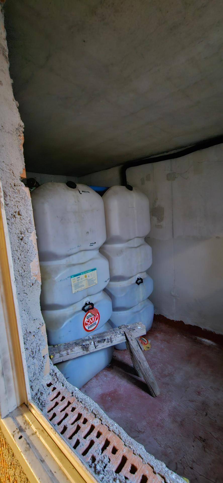 Lagerraum im Keller mit großen Wassertanks und unverputzten Wänden, durch ein Fenster sichtbar.