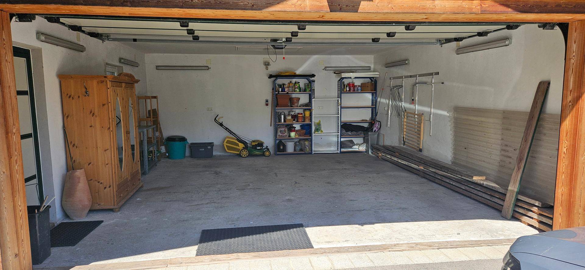 Geräumige Garage mit Betonboden, Regalen und Stauraum für Werkzeuge und Geräte.