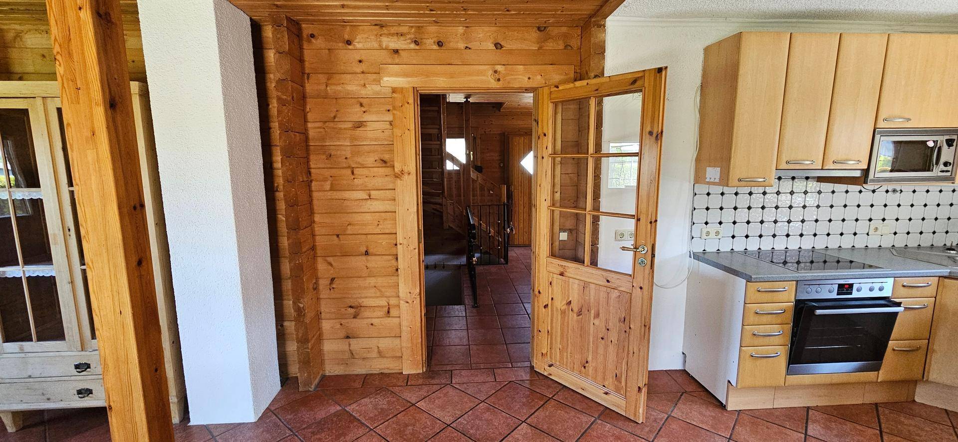 Funktionale Küche mit Holzschränken, Fliesenboden und Blick auf den Treppenaufgang.