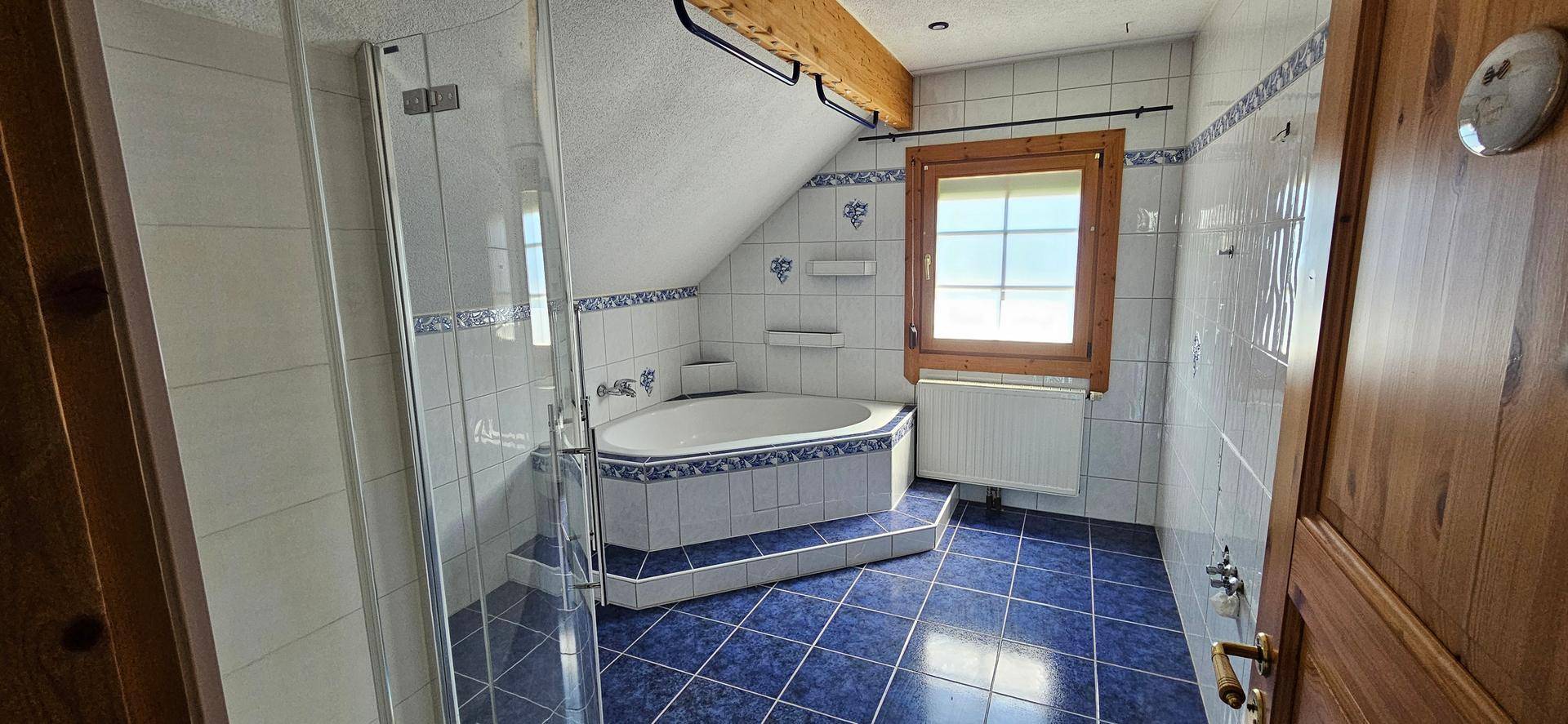 Badezimmer im Dachgeschoss mit blauen Fliesen, Badewanne, separater Duschkabine und Dachschräge.