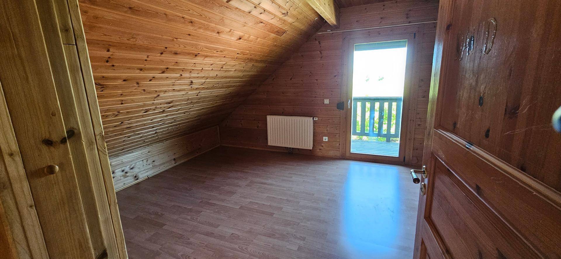 Helles Dachgeschosszimmer mit Holzvertäfelung, Laminatboden und Balkontür.
