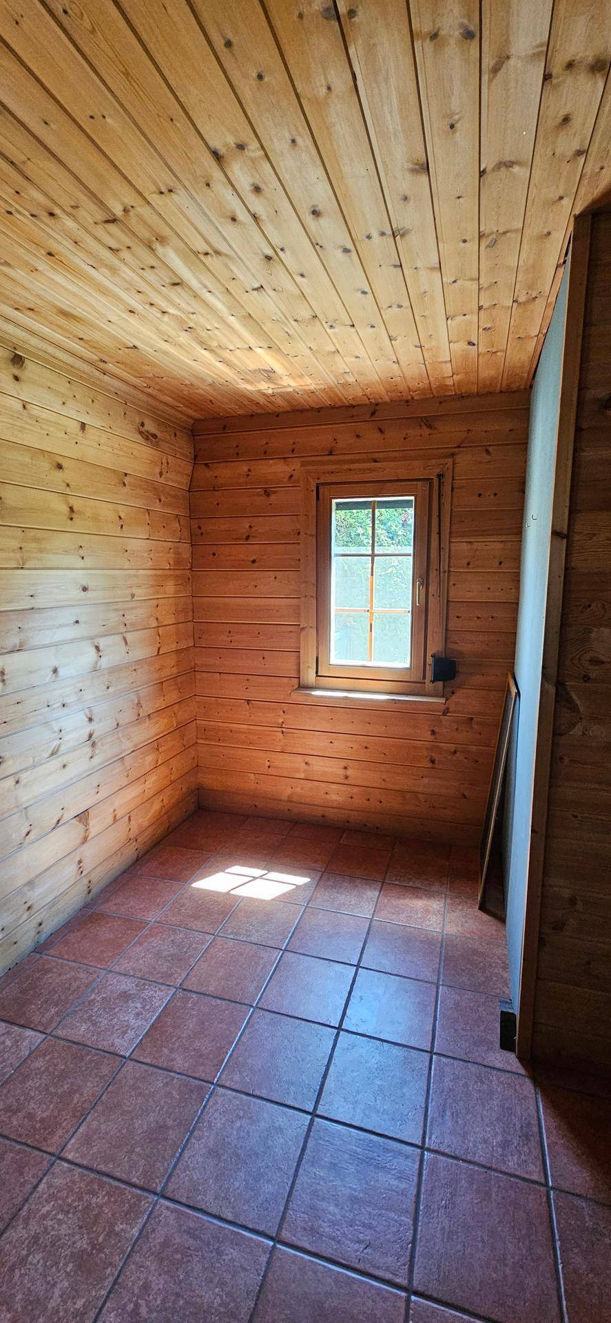 Kleiner Raum mit Holzvertäfelung, Terrakottafliesen und Fenster für Tageslicht.