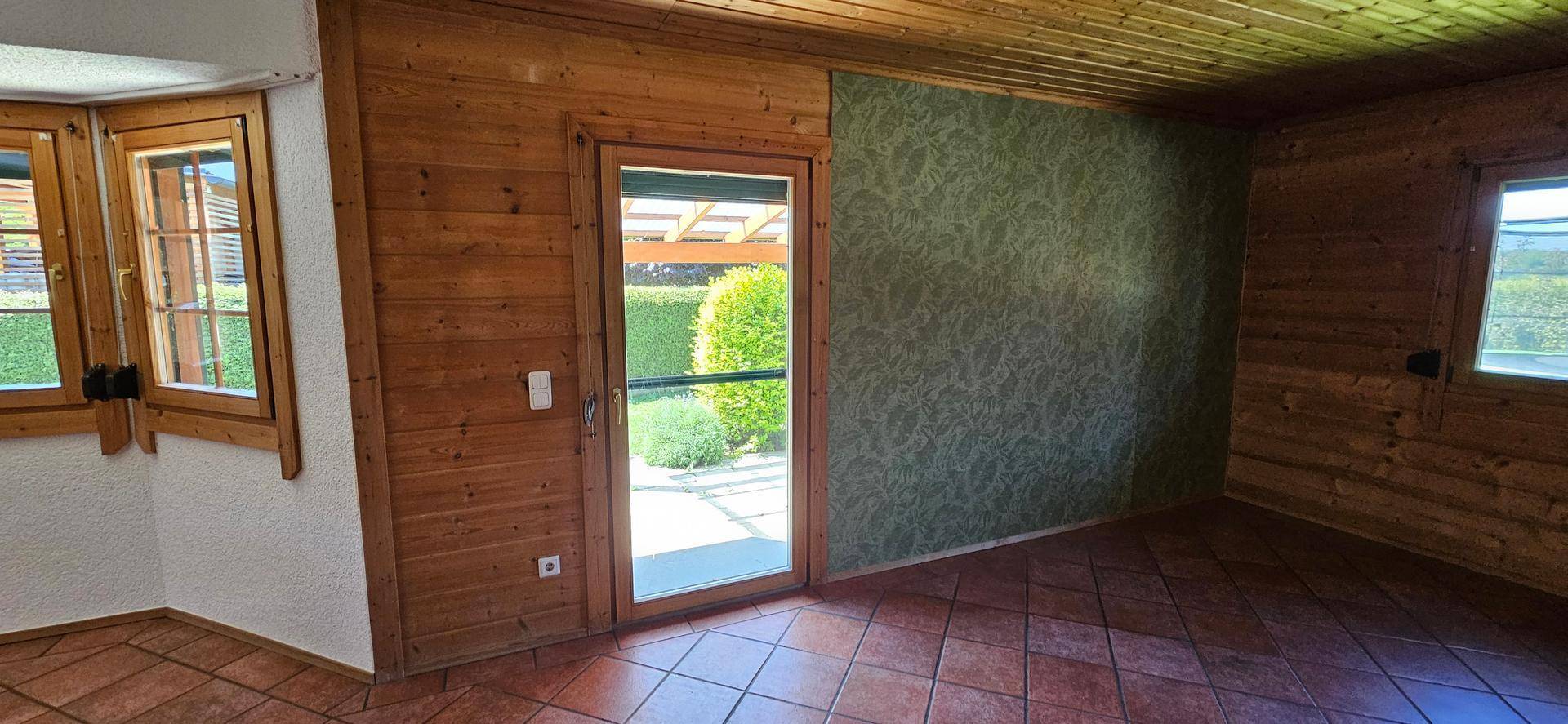 Heller Raum mit Holzvertäfelung, Terrakottafliesen und Zugang zur Terrasse oder Garten.