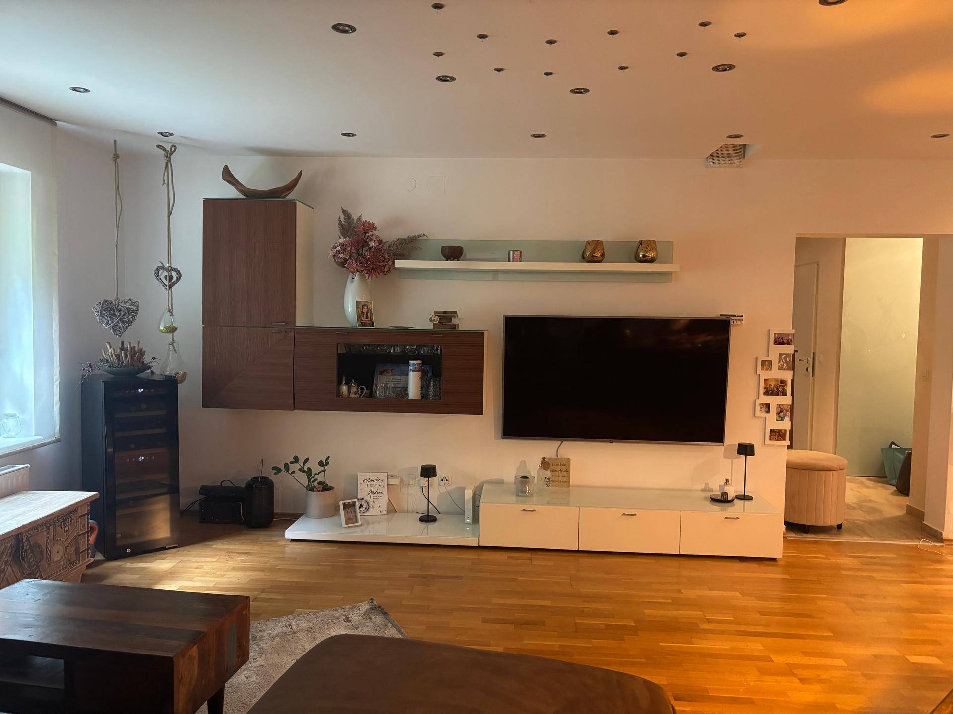 Geräumiges Wohnzimmer mit großem Fernseher, modernen Möbeln und vielen Deckenspots.