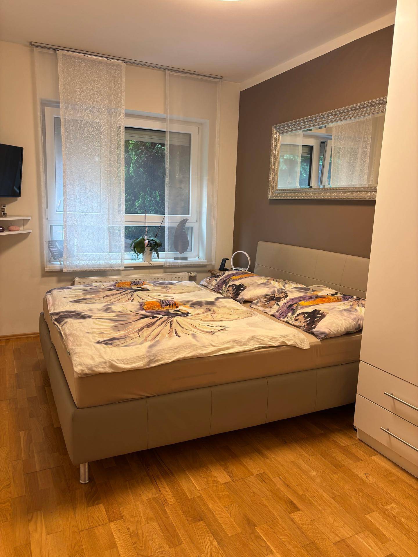 Helles Schlafzimmer mit Doppelbett, Holzboden und Fenster mit Blick ins Grüne.