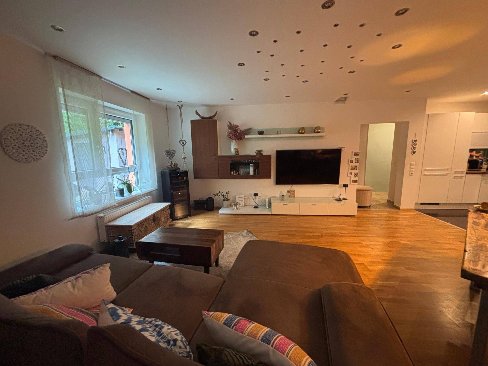 Gemütliches Wohnzimmer mit großem Sofa, Holzboden und Blick auf den Garten durch das Fenster.
