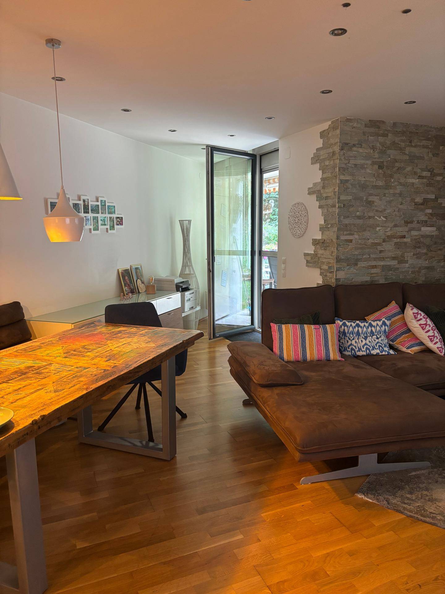 Heller Wohn-Essbereich mit Holzboden, bequemer Couch und dekorativer Steinwand.