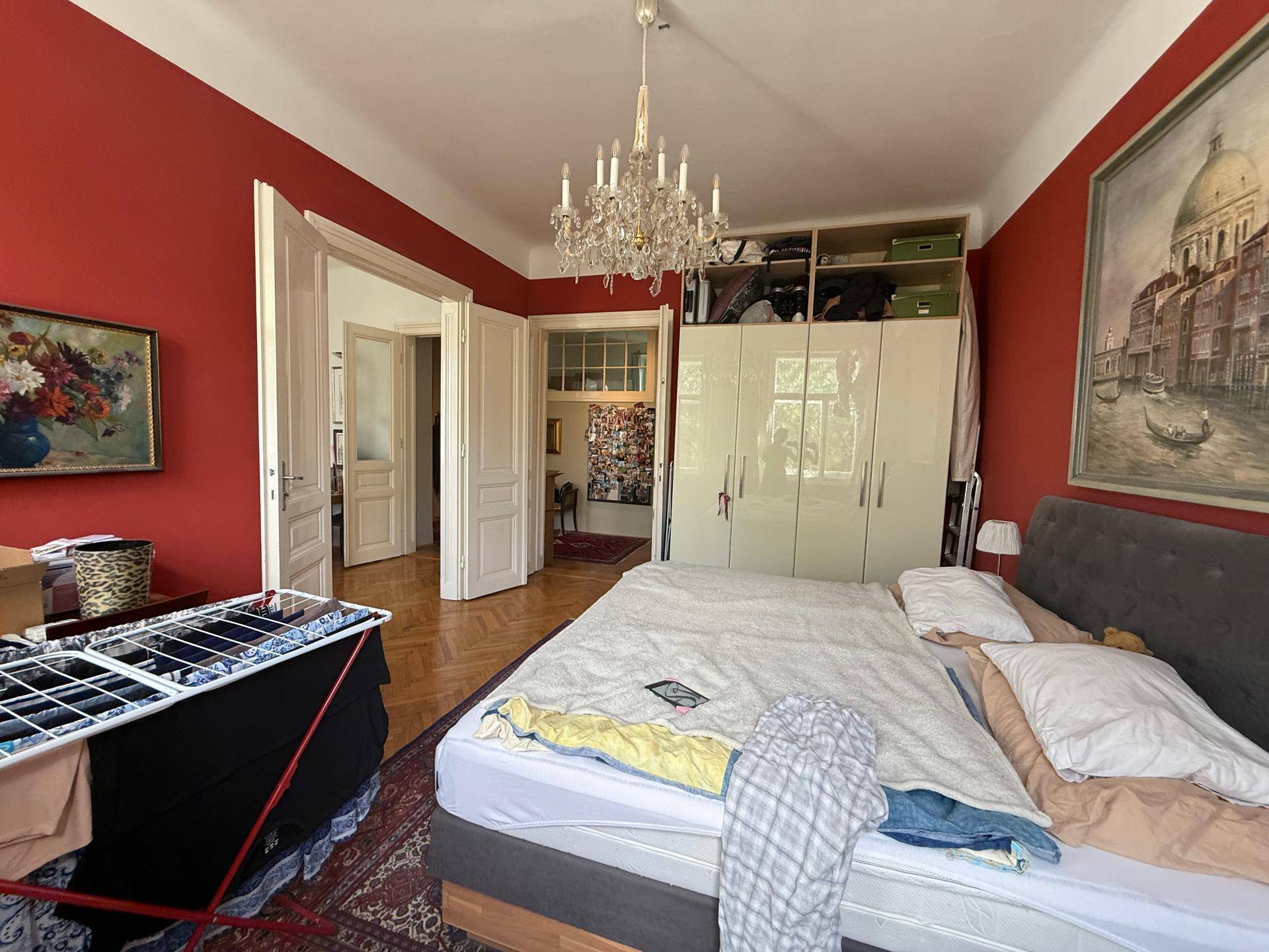 Helles Schlafzimmer mit roten Wänden, großem Kleiderschrank und Zugang zu weiteren Räumen.