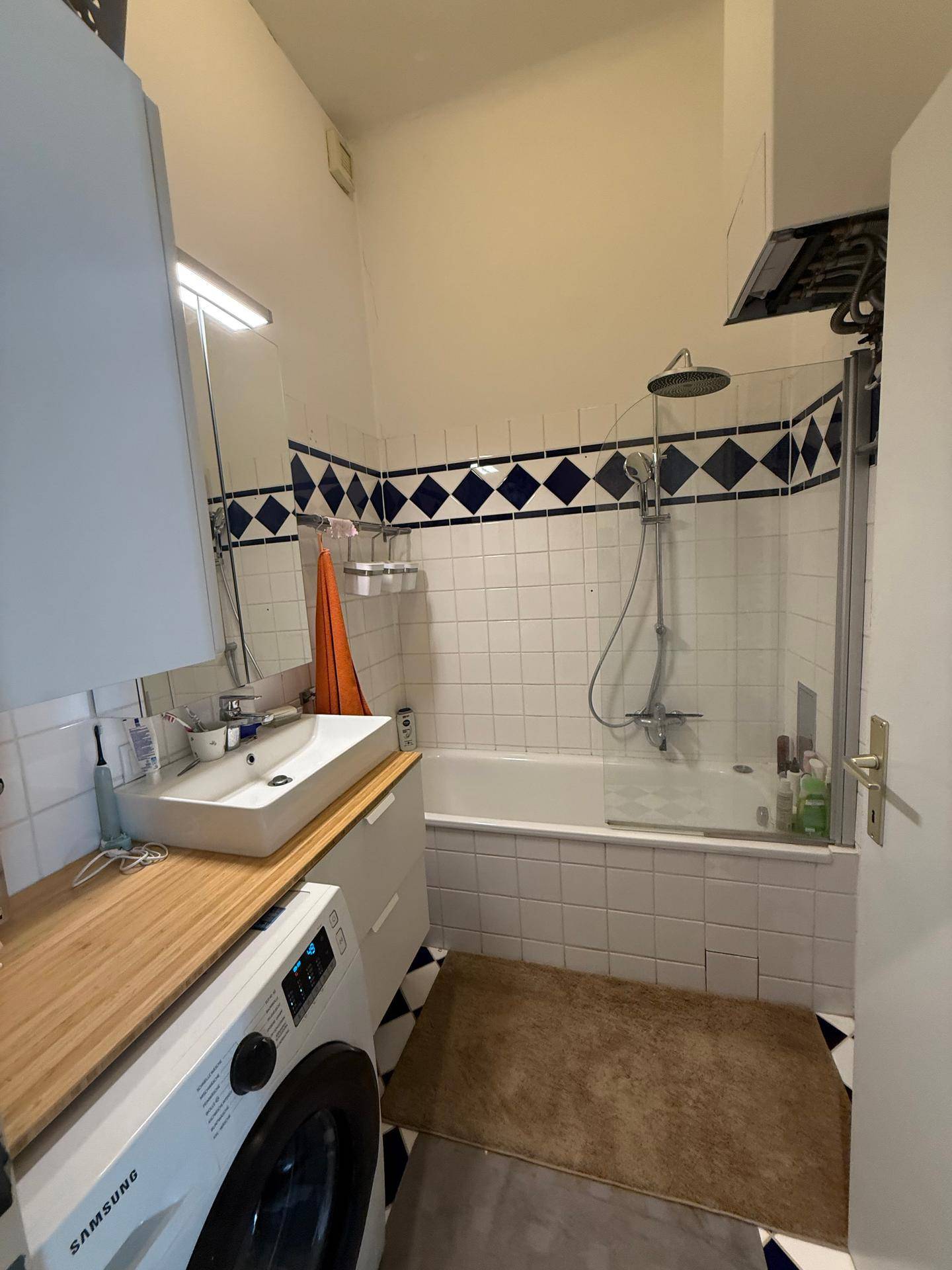 Badezimmer mit Badewanne, Dusche, Waschbecken und Waschmaschine, gefliest in Weiß und Blau.