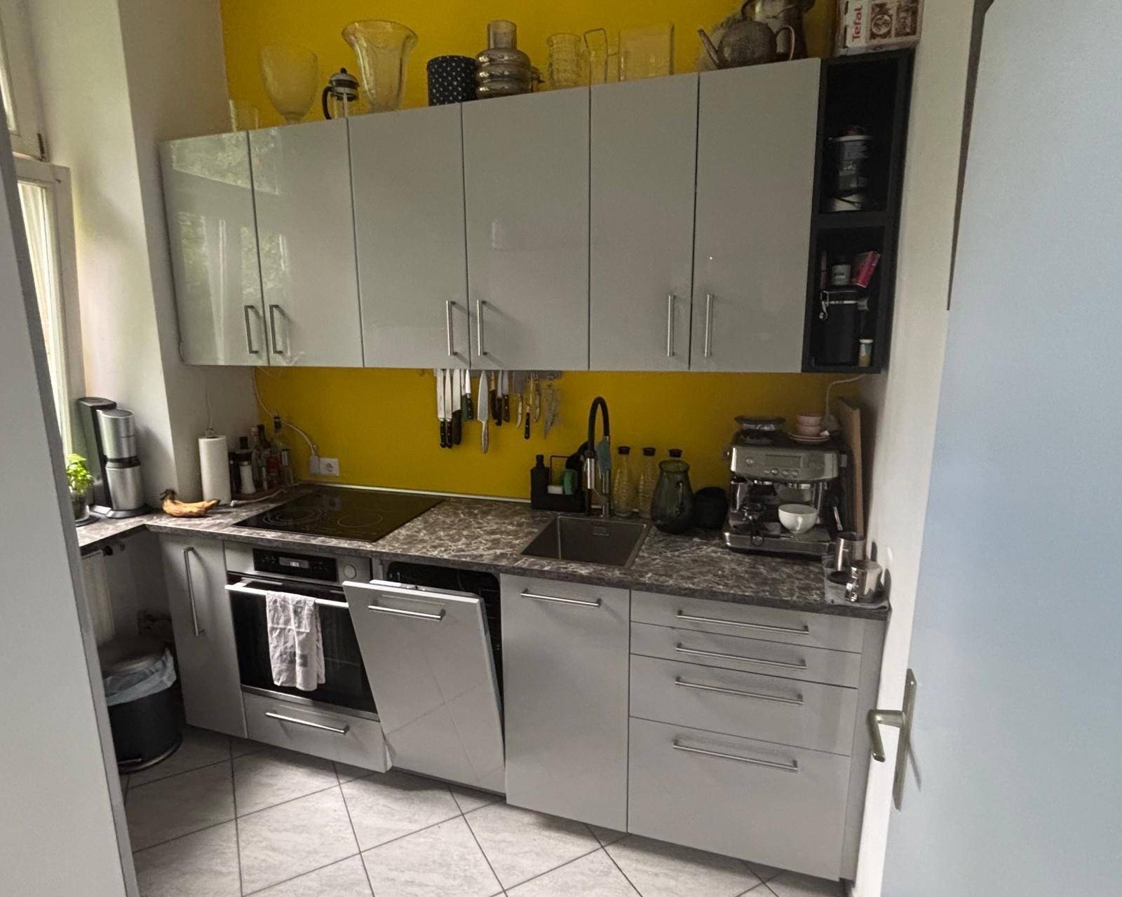 Moderne Küche mit grauen Hochglanzschränken, gelber Wand und Fliesenboden.