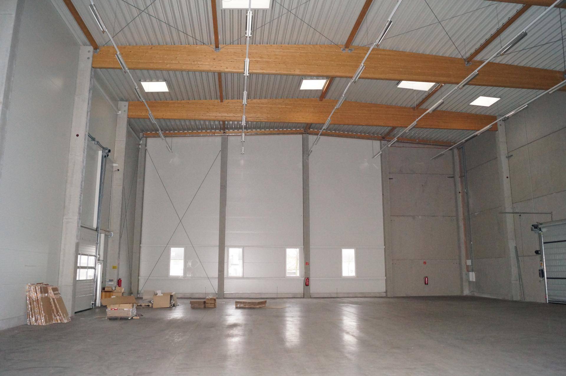 Große, leere Lagerhalle mit hohen Decken, Holzbalken und Oberlichtern, viel Platz.