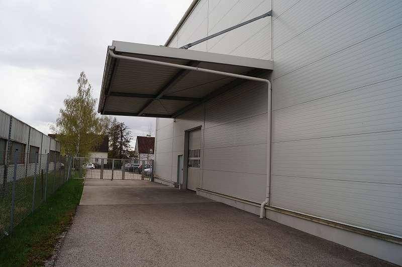 Überdachter Eingangsbereich mit Rolltor und Zufahrt zu einer Lagerhalle.