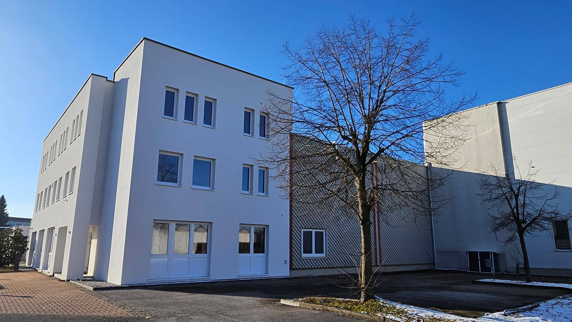 Ansicht des modernen Bürogebäudes mit angrenzender Lagerhalle und kahlen Bäumen im Winter.