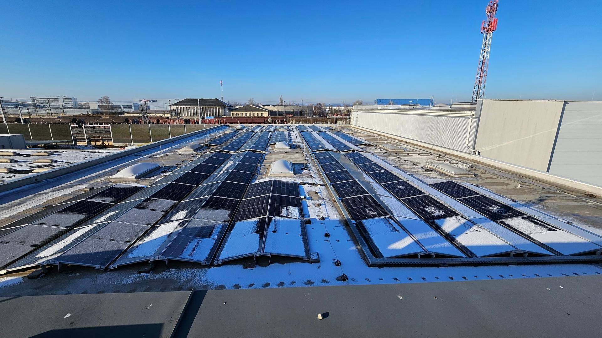 Dachansicht mit zahlreichen Photovoltaik-Modulen, teilweise mit Schnee bedeckt, unter blauem Himmel.