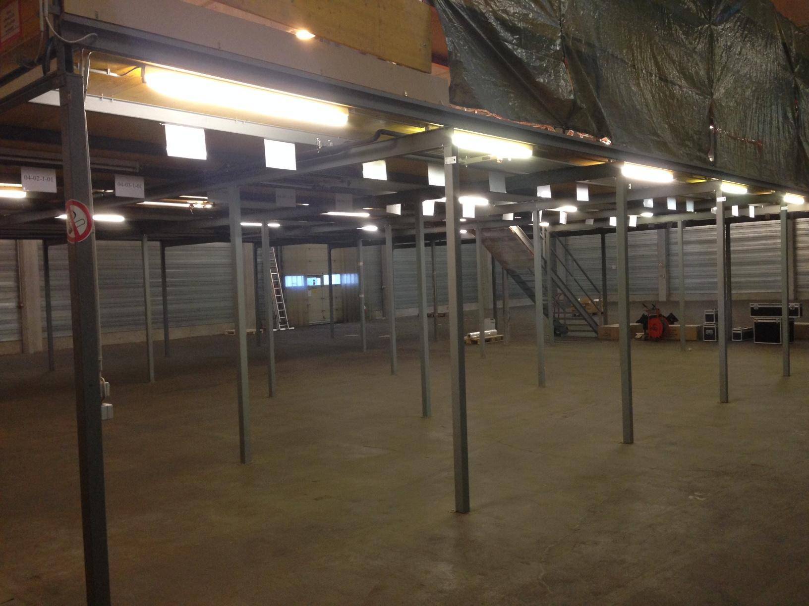 Lagerhalle mit Zwischengeschoss-Konstruktion aus Metall und Holz, mit Beleuchtung und Treppe.