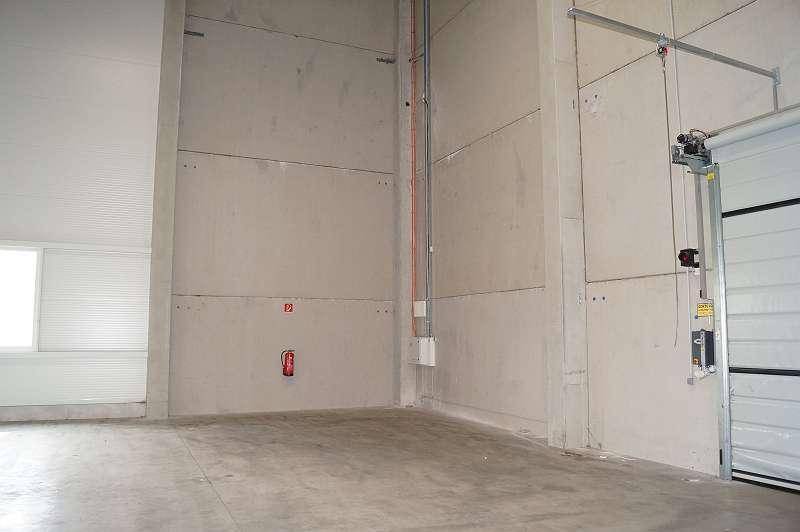 Ecke einer Lagerhalle mit Betonwänden, sichtbaren Leitungen und einem Rolltor.