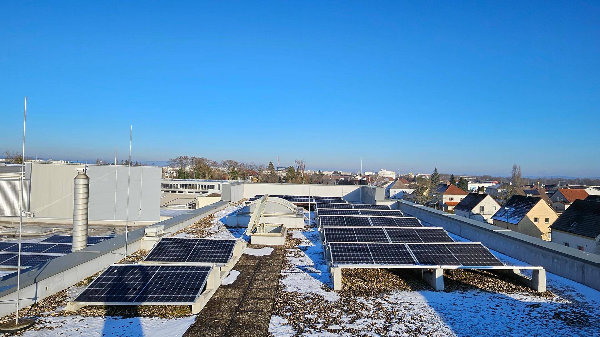 Weitläufige Dachfläche mit Photovoltaik-Modulen und Blick auf die umliegende Bebauung.