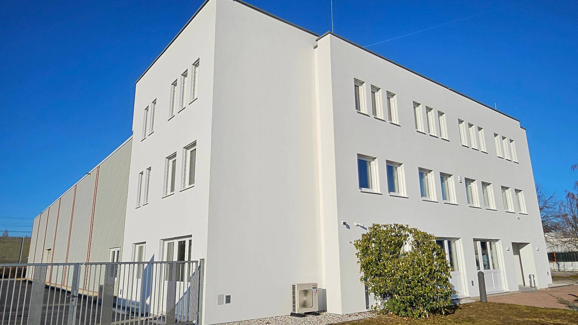 Seitenansicht des modernen Bürogebäudes mit weißer Fassade, Fenstern und einer Außeneinheit.