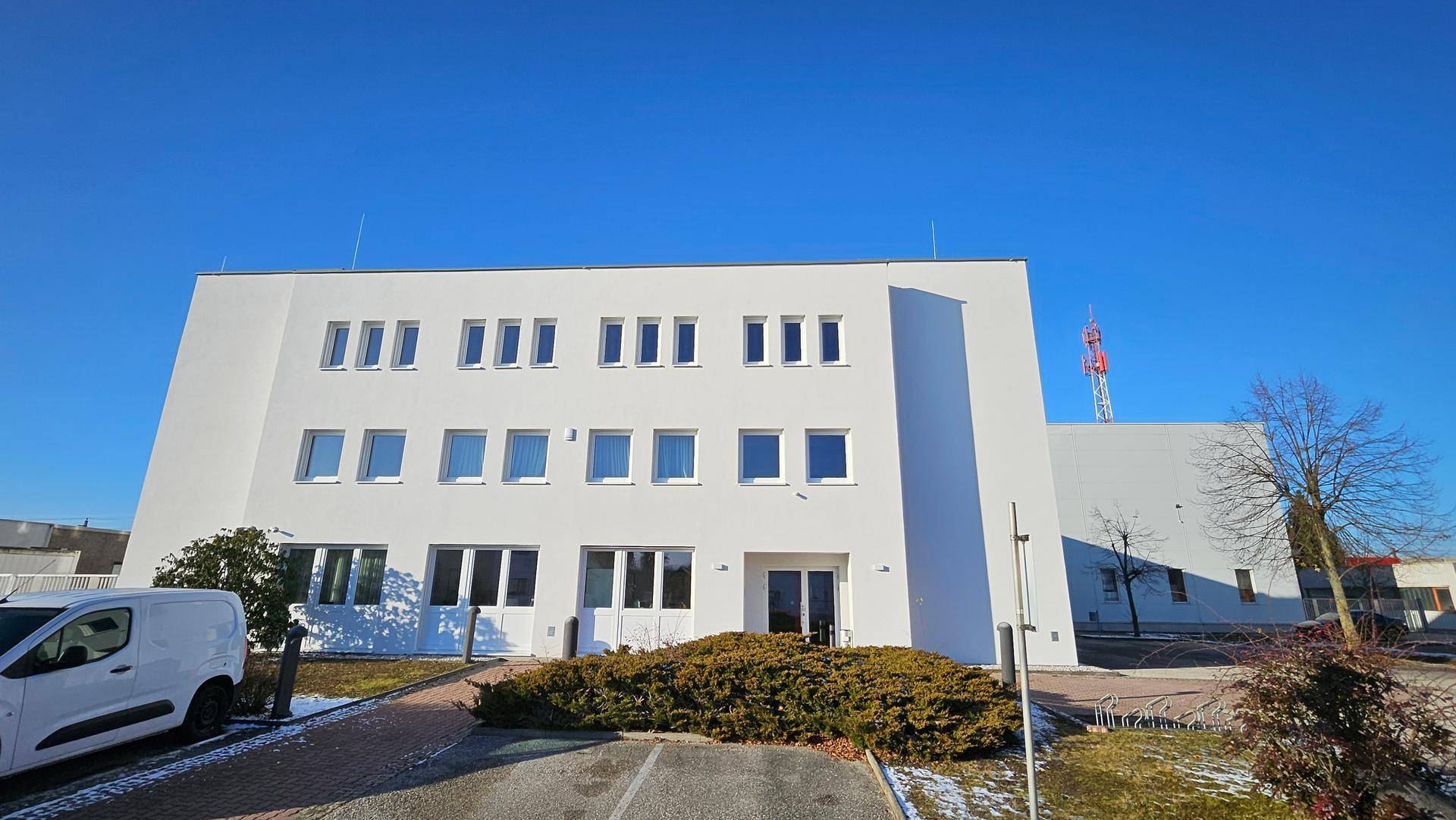 Frontansicht des modernen Bürogebäudes mit weißer Fassade, vielen Fenstern und einem Lieferwagen.