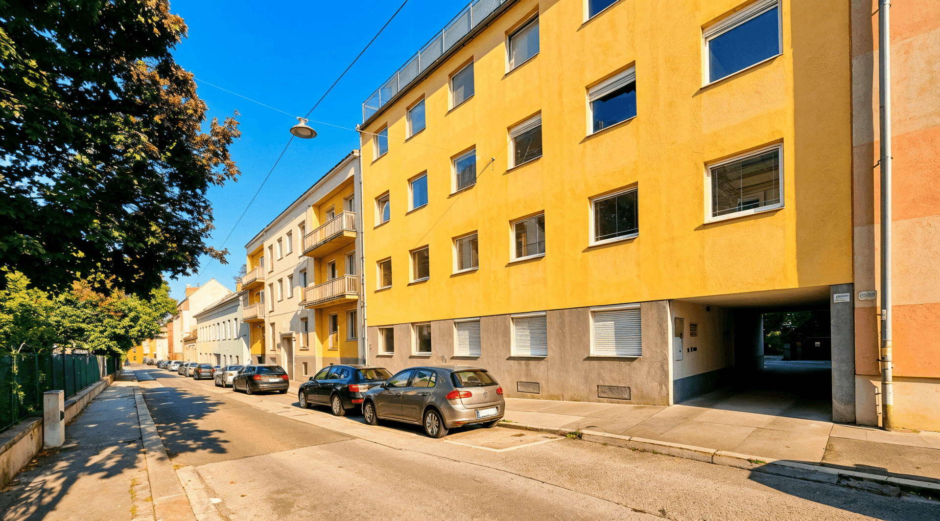 Gelbes Mehrfamilienhaus an einer ruhigen Straße mit parkenden Autos.