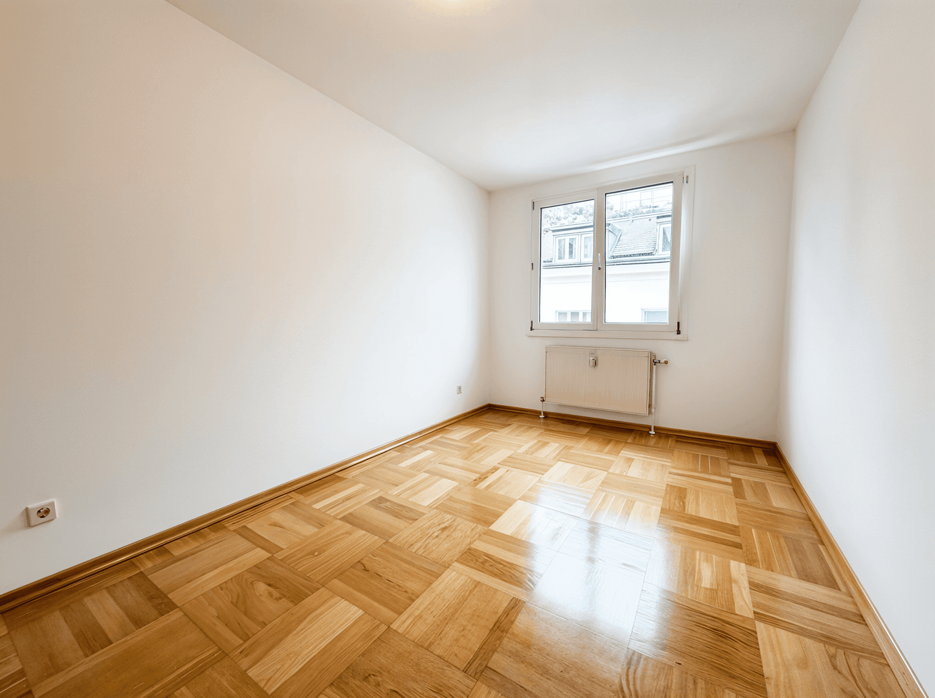 Leeres Schlafzimmer mit Parkettboden und Fenster, bereit zur individuellen Gestaltung.