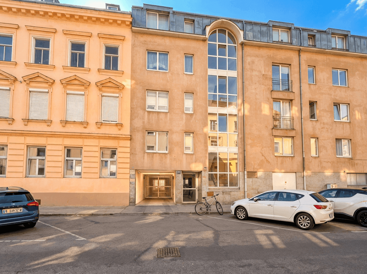 Wohngebäude mit unterschiedlichen Fensterformen und geparkten Autos auf der Straße.